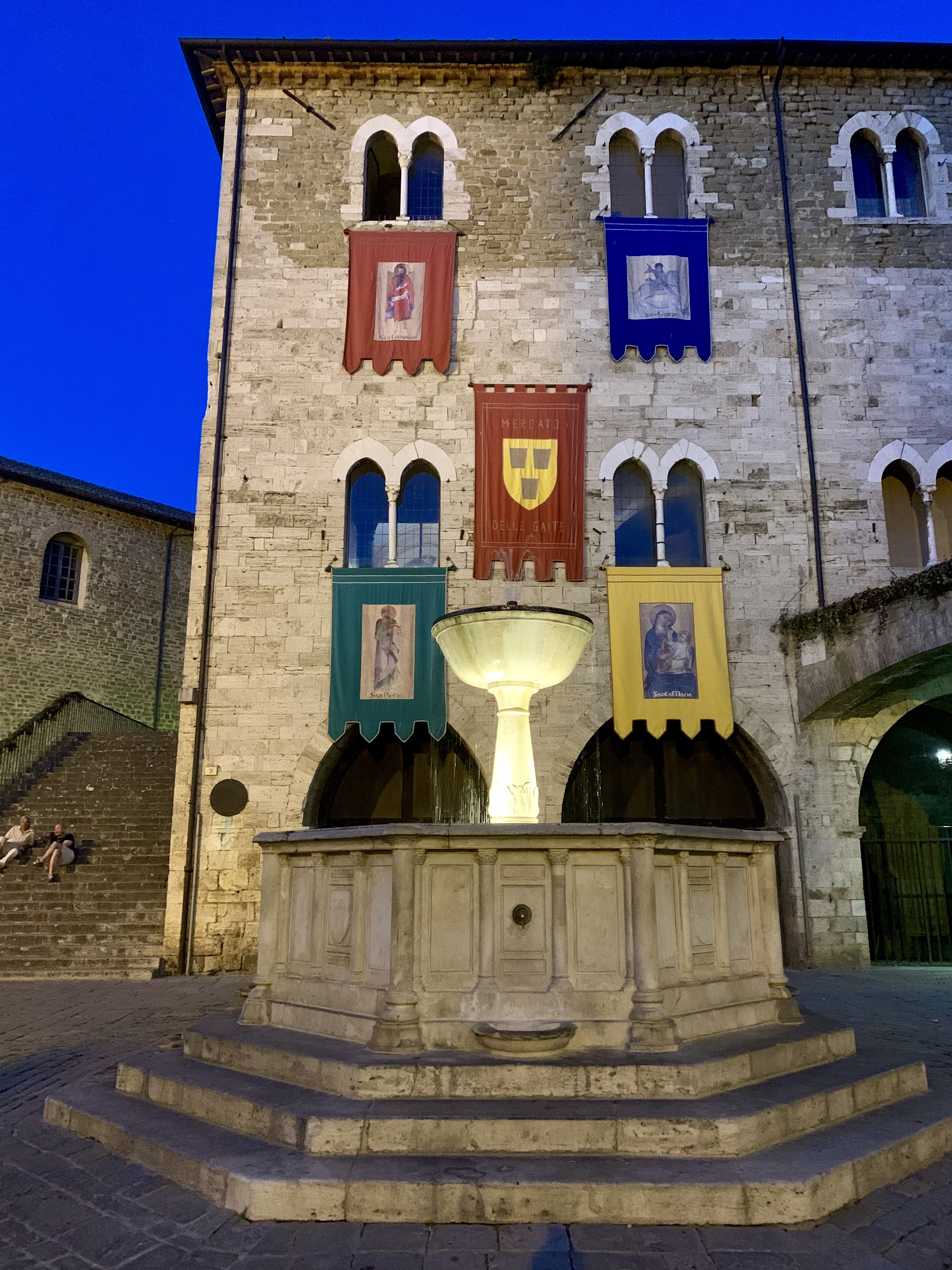 The wall of colorful banners, over a lit-up fountain after sunset