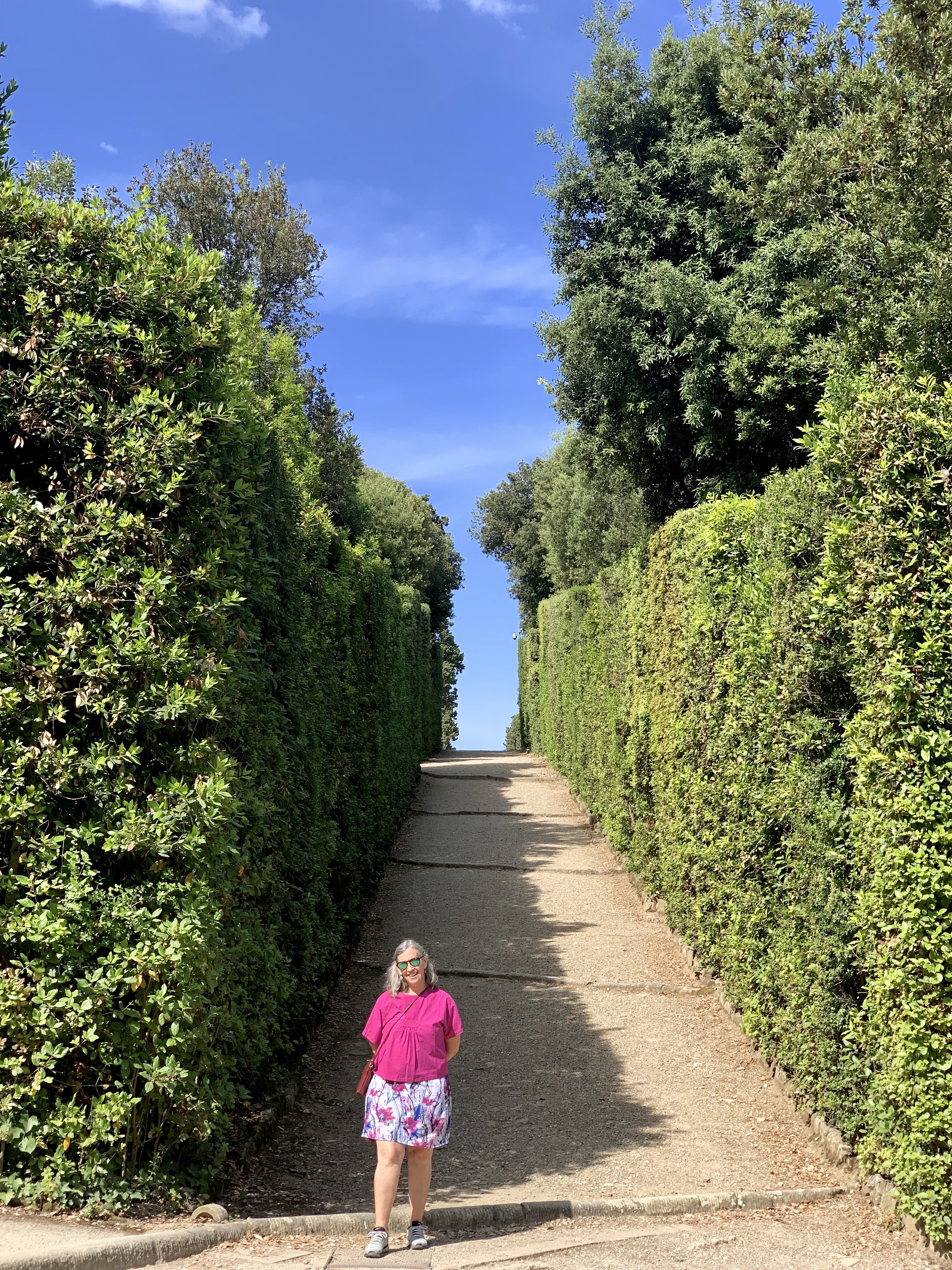 Mallory next to a towering hedge, under an azure sky